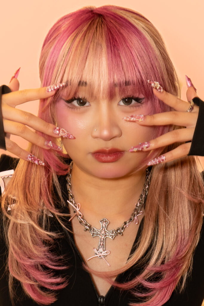 Beauty-Portrait einer Person mit pink-blonden Haaren und aufwendigem Nail-Art Styling vor hellem Hintergrund.
