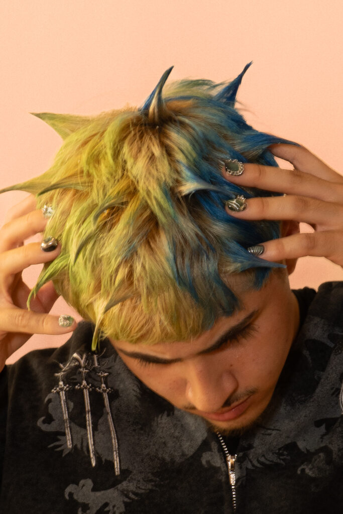 Editorial-Portrait mit bunt gefärbten Haaren und avantgardistischem Styling in warmer Studiobeleuchtung.