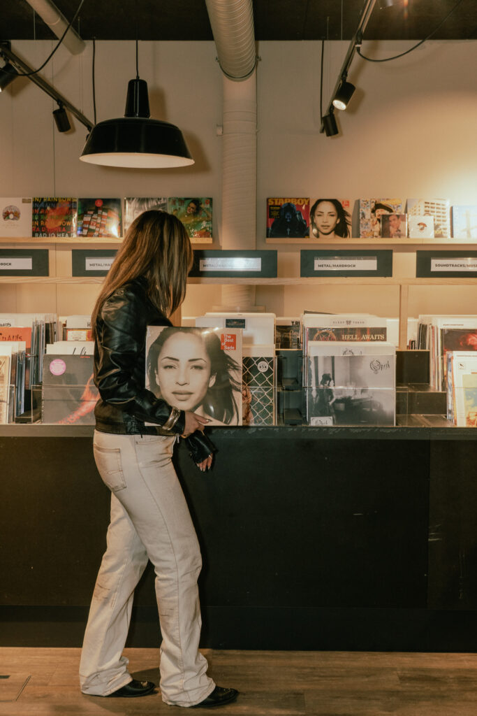 Eine Frau steht vor einem Regal voller Vinylplatten in einem modernen Record Store und betrachtet ein Albumcover.